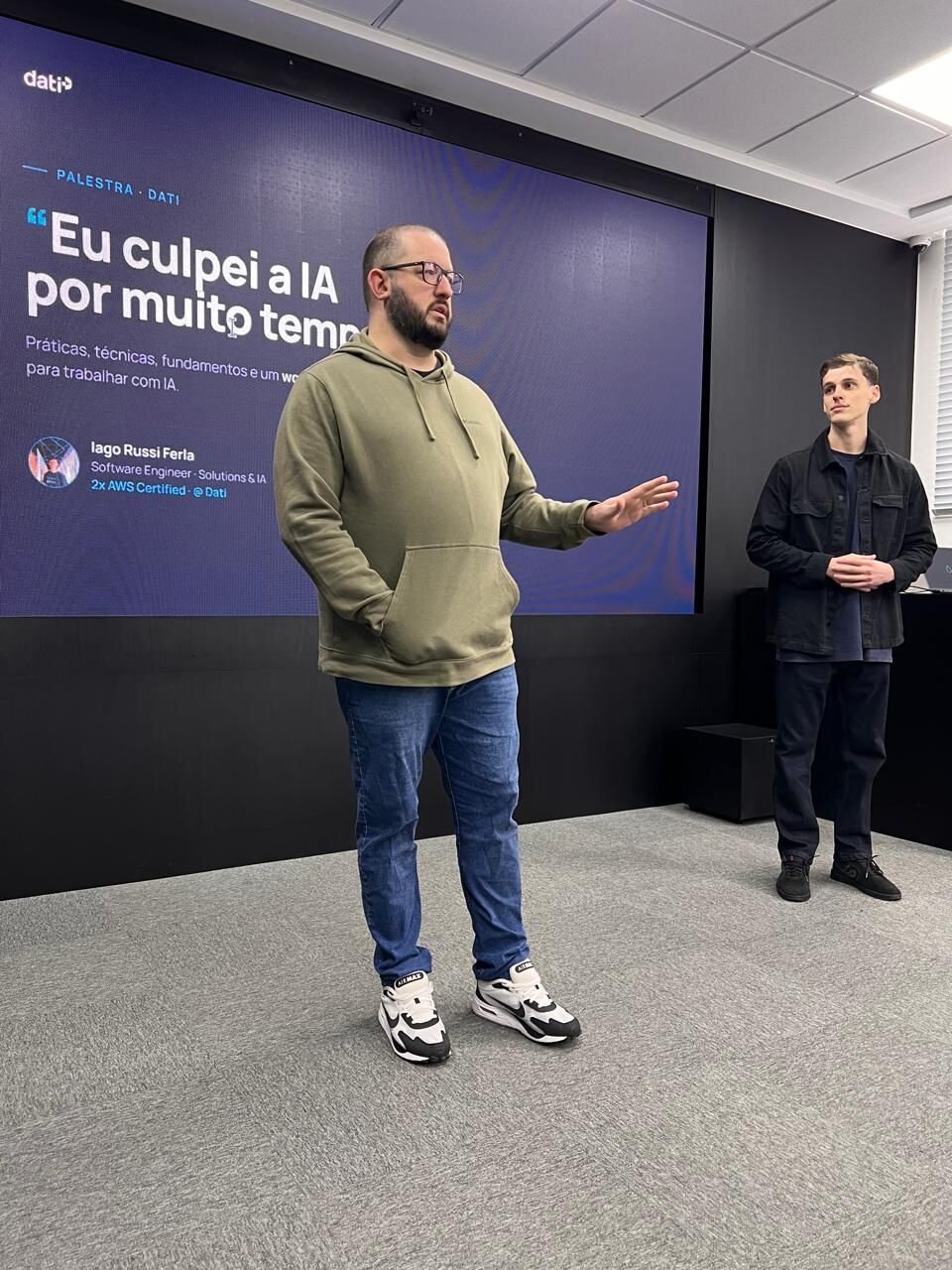 Palestra na Dati com o slide "Eu culpei a IA por muito tempo", com Iago de pé à direita
