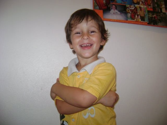 Iago criança, de camiseta amarela, sorrindo de braços cruzados