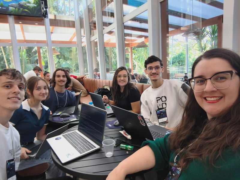 Selfie do grupo com notebooks abertos numa mesa, durante o hackathon