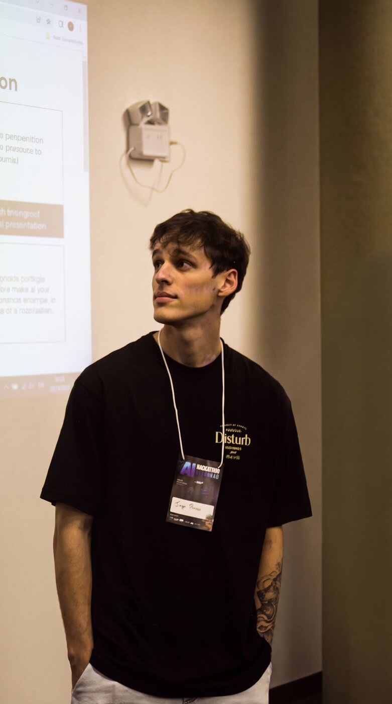 Iago de camiseta preta e crachá do AI Hackathon, olhando para o lado, em frente a uma projeção